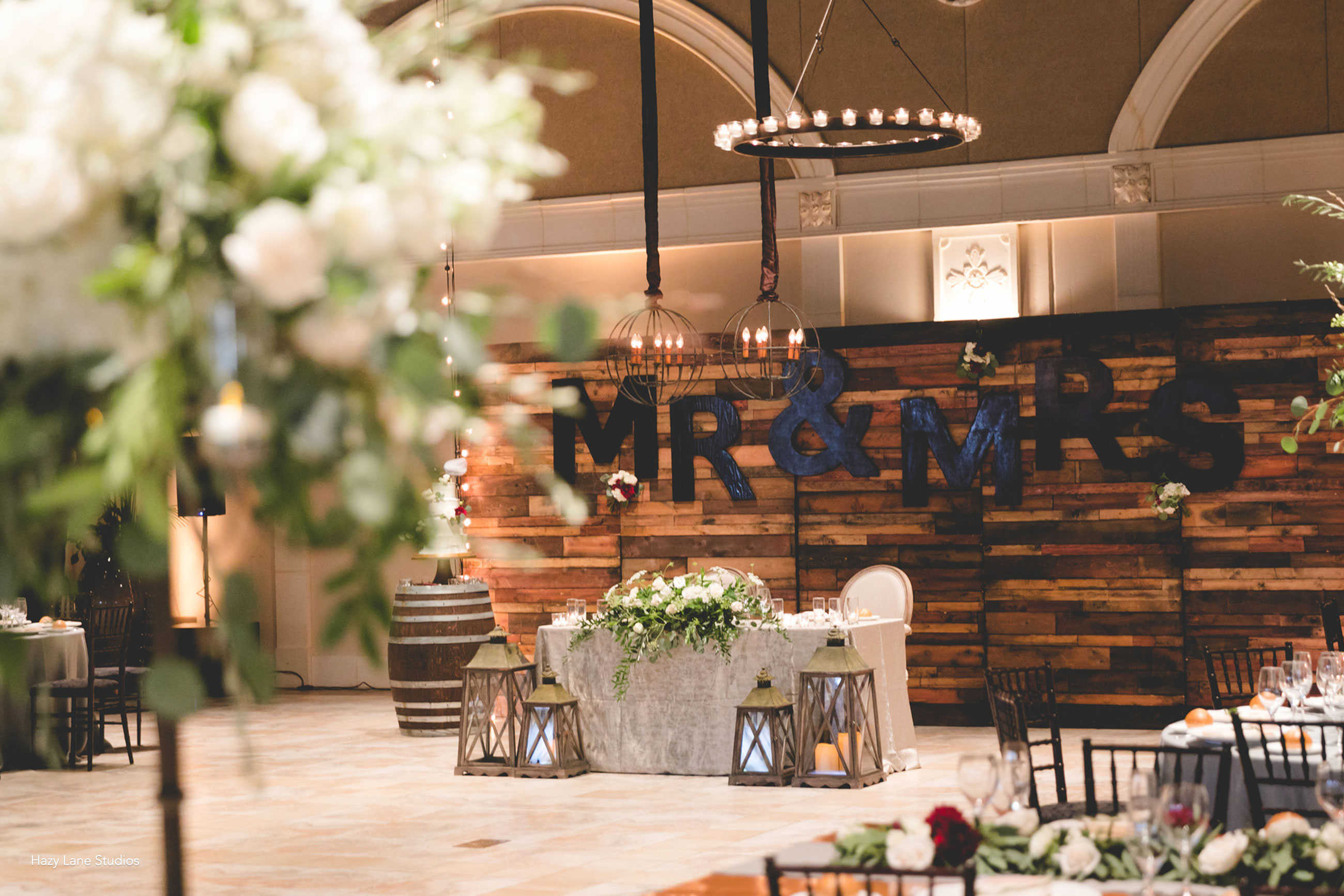 Unique wedding reception with sweetheart table wood wall backdrop at Casa Real at Ruby Hill Winery (www.casarealevents.com).  Photo by: Hazy Lane Studios; Florals: Michael Daigian Design; Lighting and Wall: Fantasy Sound Event Services 